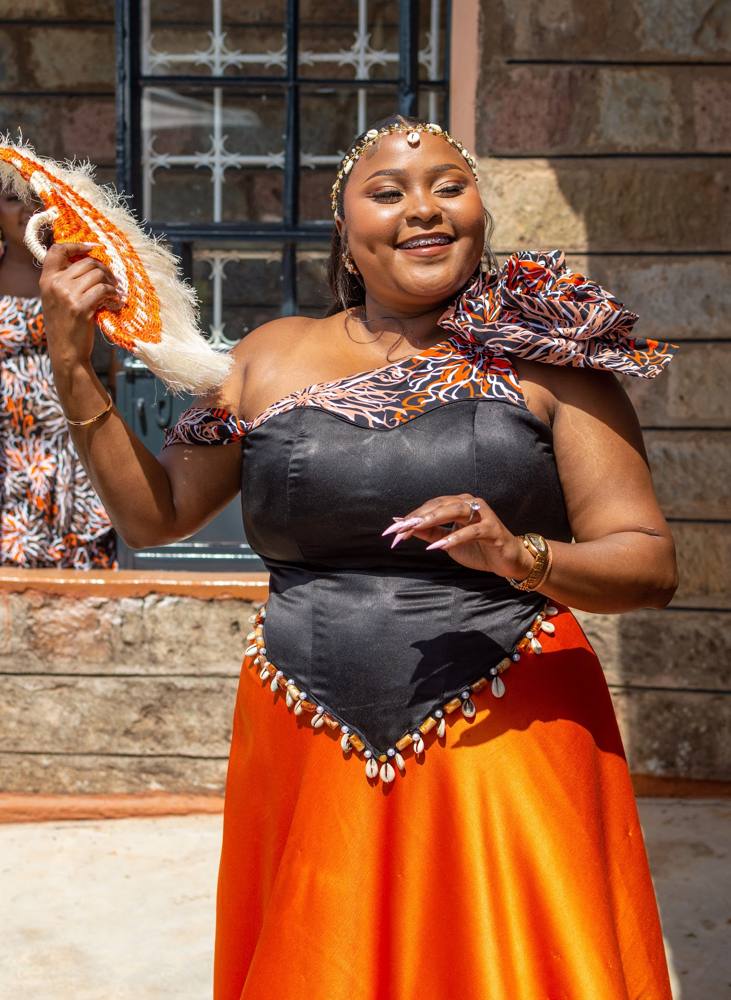 A bride in a custom orange and black Ankara ruracio outfit